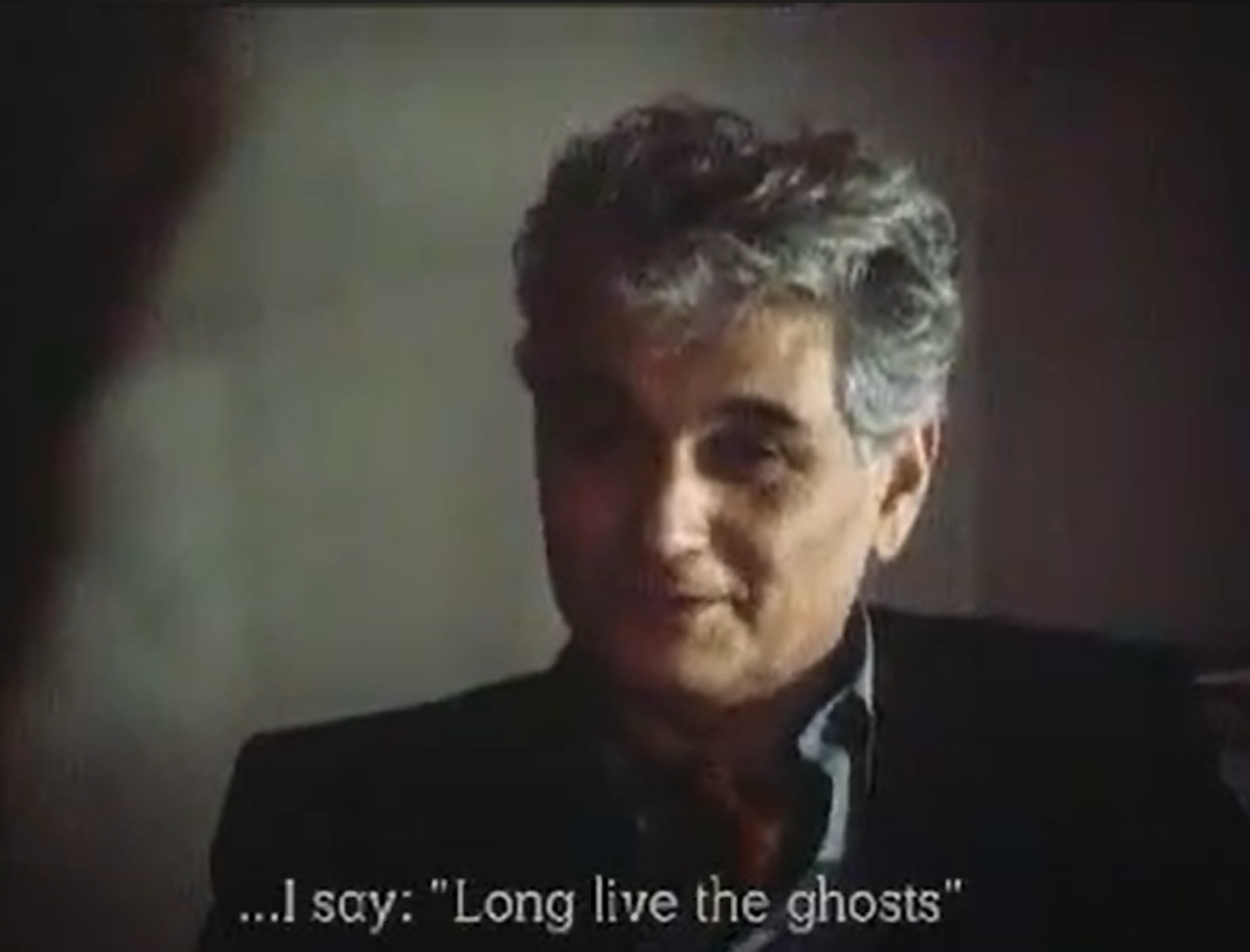 screenshot of the 1983 film Ghost Dance directed by Ken McMullen. The screenshot features a grainy middle-aged man (Jacques Derrida), and the caption '...I say: Long live the ghosts'
